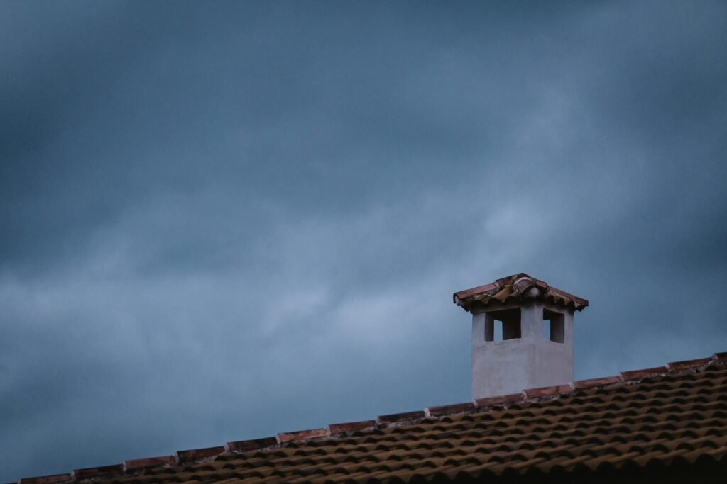 A rooftop chimney with tiled roof under a dramatic cloudy sky during twilight. Chimney service in East Rutherford NJ